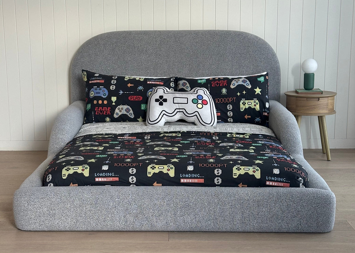 Gray kids bed with a pillow featuring gaming controller designs on a wooden floor.