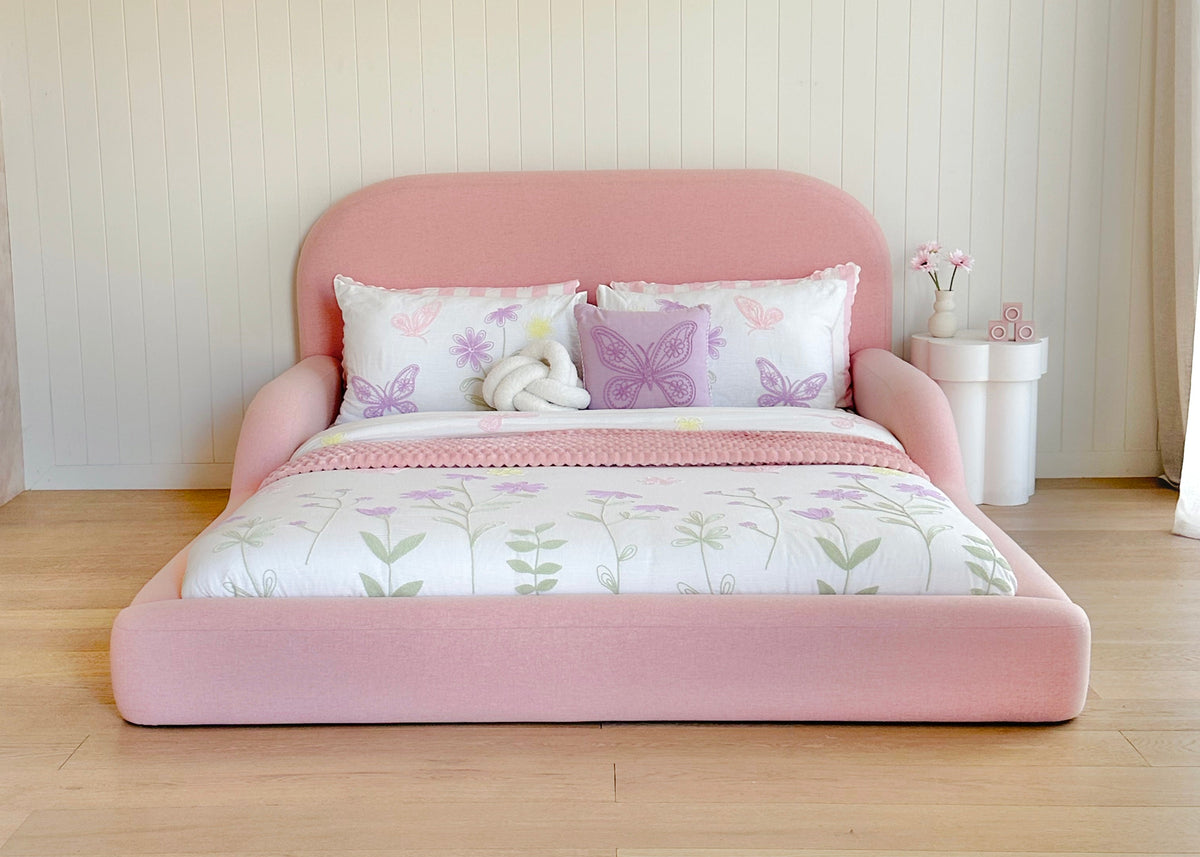 Pink bed with butterfly-patterned bedding in a room with light wood flooring and white walls.