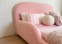 Pink bed with striped pillows against a white paneled wall