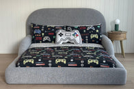 Gray kids bed with a pillow featuring gaming controller designs on a wooden floor.