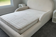 White upholstered headboard against a gray wall with a window in the background