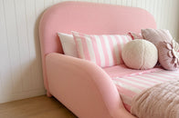 Pink bed with striped pillows against a white paneled wall