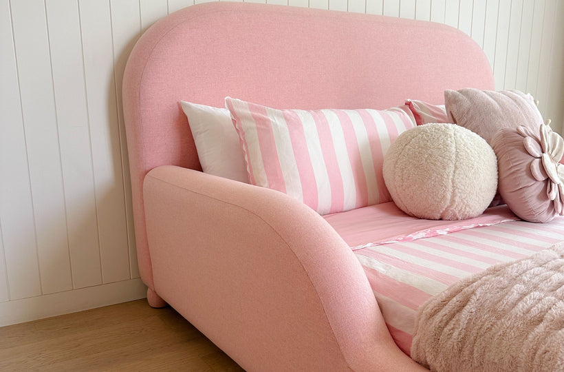 Pink bed with striped pillows against a white paneled wall