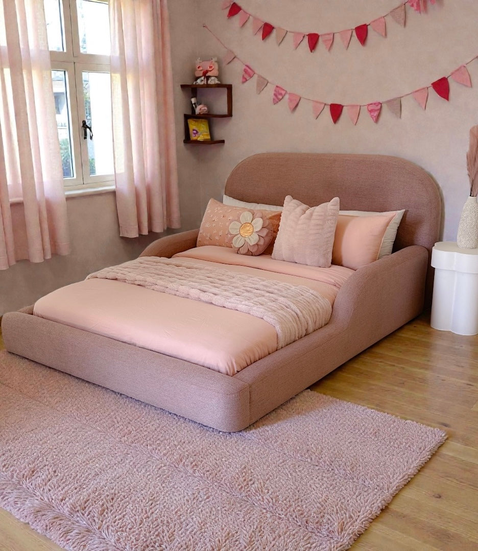 Pink bed in a room with a window, shelves, and decorative flags.